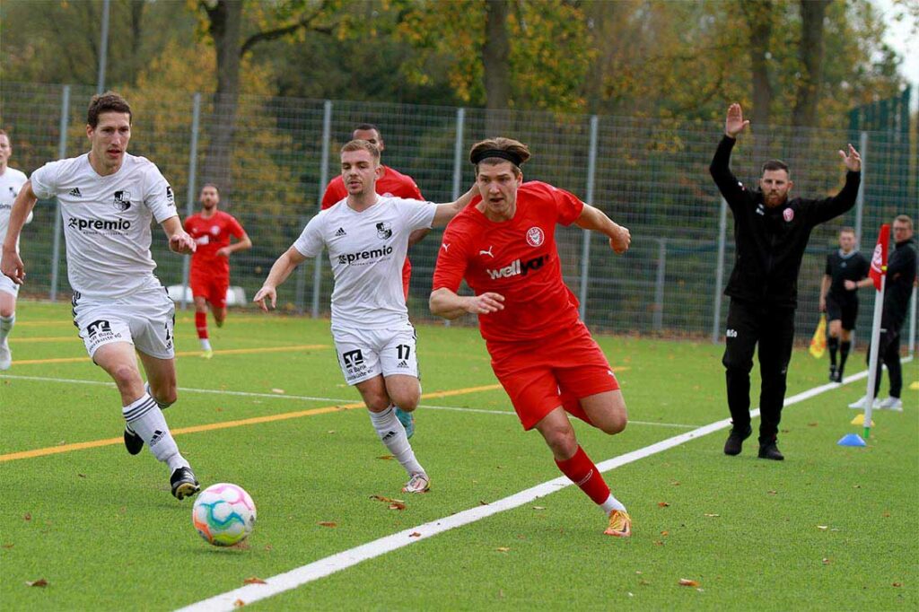 Jan Matti Seidel (in rot, FC Kilia Kiel), der an der Seitenlinie versucht, David Quade (li., Heider SV) und Lennart Busch) abzuhängen, erzielte das 1:1. © 2022 Ismail Yesilyurt