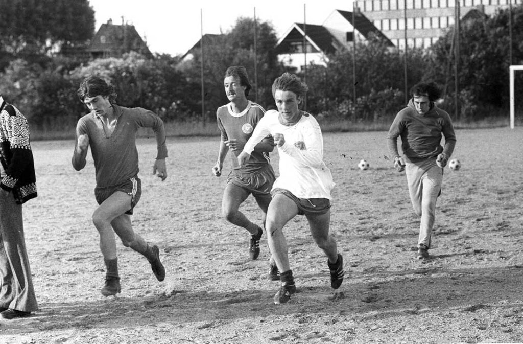 Saisonvorbereitung 1974 auf dem staubigen und trockenen Fögeplatz, Blickrichtung Projensdorfer Straße. Dietmar Tönsfeldt und Thorsten Neumann sprinten vor Dieter Reh und Egbert Landsberg. Der Hammerwurfkäfig, der sich ungefähr hinter Tönsfeldt befand, ist nicht mehr vorhanden. Quelle Stadtarchiv Saisonvorbereitung 1974 auf dem staubigen und trockenen Fögeplatz, Blickrichtung Projensdorfer Straße. Dietmar Tönsfeldt und Thorsten Neumann sprinten vor Dieter Reh und Egbert Landsberg. Der Hammerwurfkäfig, der sich ungefähr hinter Tönsfeldt befand, ist nicht mehr vorhanden.