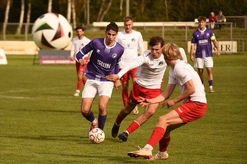 Ilir Serifi (VfR Neumünster) am Ball gegen zwei Spieler des VfB Lübeck II (Szene aus Hinspiel Saison 2024/25). © 2024 Olaf Wegerich